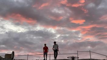 Sunset, clouds, and two individuals silhouetted on a levee
