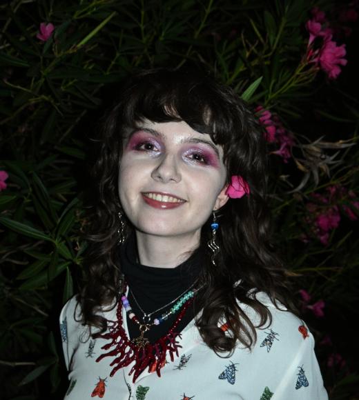Smiling young woman with pink eyeshadow, nighttime photo in front of pink Oleanders