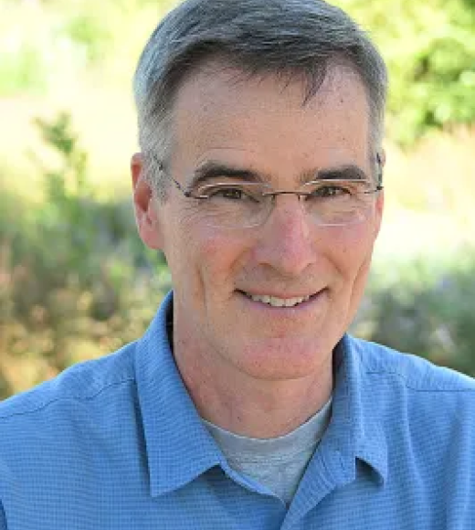 Smiling middle-aged man with glasses, blue shirt, outdoor headshot